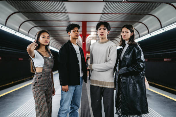 Four stylish young adults confidently pose in trendy clothing on a subway platform, highlighting fashion's role in identity.