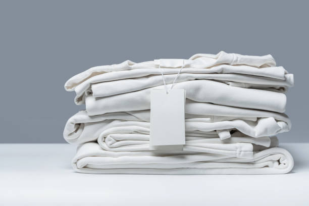 Stack of white clothing with a blank tag against a gray background, illustrating the role of color in fashion.